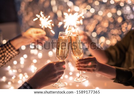 Hands of couple clinking with flutes of champagne and their friends holding sparkling bengal lights Royalty-Free Stock Photo #1589177365
