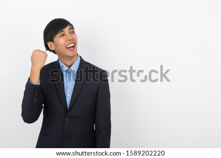 Excited young business Asian man raising his fists with happy delighted face, celebrating success isolated on white background.