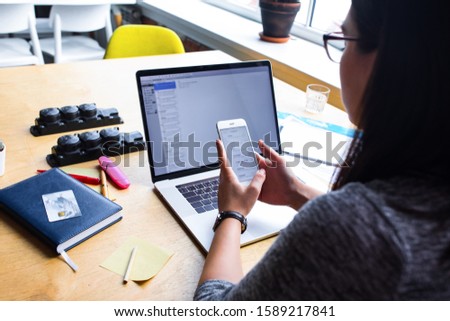 Business woman reading text message on mobile phone during work on pc laptop computer, sitting at wooden table in office interior. Female bookkeeper online booking on cellphone  Royalty-Free Stock Photo #1589217841