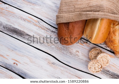 Different kinds of bread in burlap bag on wooden table. Healthy farmers bread. Space for text.