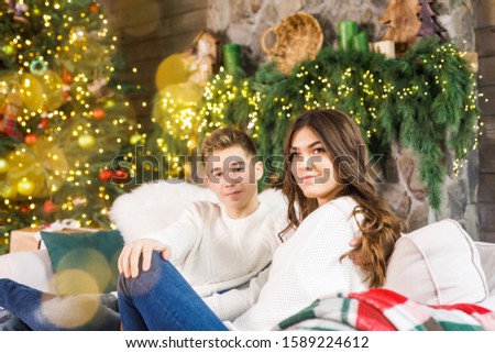 young beautiful couple sitting in a beautiful room on the bed against the background of the Christmas tree and smiling