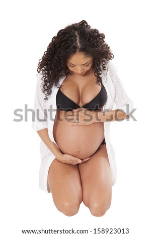 A woman in her 8th month of pregnancy looks down at her baby bump, isolated on white background.