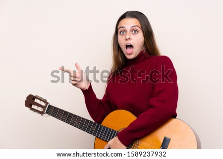 Teenager girl with guitar over isolated background surprised and pointing side