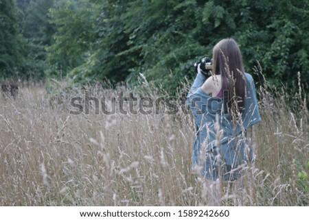Female woman photographer taking photograph in tall grassy country field