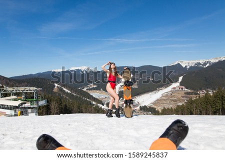 girl in a red bathing suit and glasses for a snowboard on the hillside. fitness model at a winter resort. Girl holds snowboard