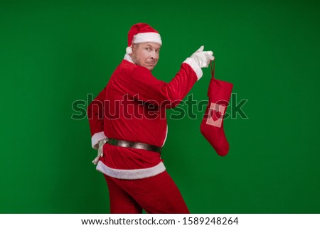 Emotional Santa Claus holds a Christmas sock for gifts in his hands and poses on a green chroma background