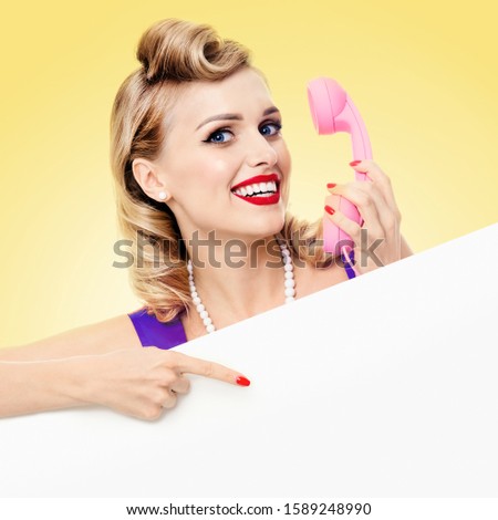 Woman with phone, in pin up style, showing blank signboard with copy space, over yellow background. Caucasian blond model in retro fashion and vintage picture. Square composition.