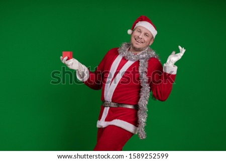 Emotional male actor in a costume of Santa Claus holds a small red gift box in his hands and poses on a green chrome background