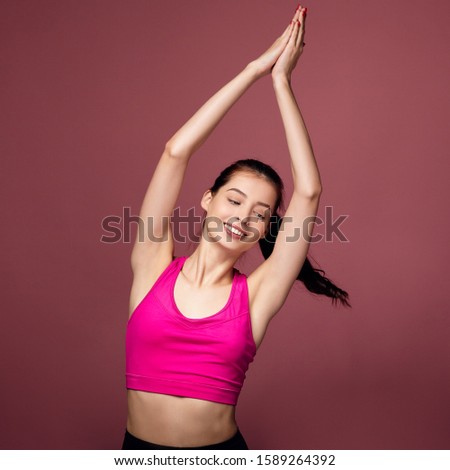 Cute sophisticated lady in a sports pink top and black leggings covered her eyes, extended her arms up and enjoys doing gymnastics. The girl does exercises, sports exercises. Photo on a background.