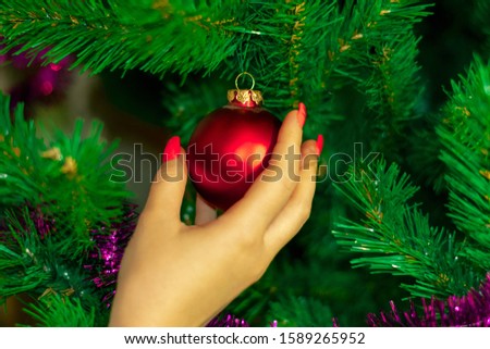 A woman decorates a Christmas tree. Female hand hangs a toy on the Christmas tree