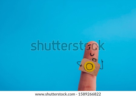 Funny finger tourist holding a camera and smiling against blue background with copy space for ad text