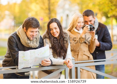 holidays and tourism concept - group of friends or couples with tourist map and camera in autumn park