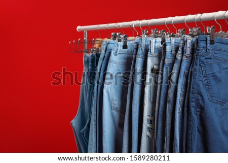 Rack with different jeans on red background