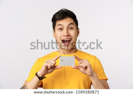 Check out this bank offer. Excited smiling and amused young asian man promote banking service, holding credit card, advice get account, paying with cashback, standing white background