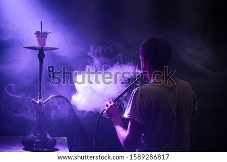 The man Smoking the classic Shisha. Beautiful background, with colored rays of light and smoke. The concept of hookah Smoking. Space for text.
