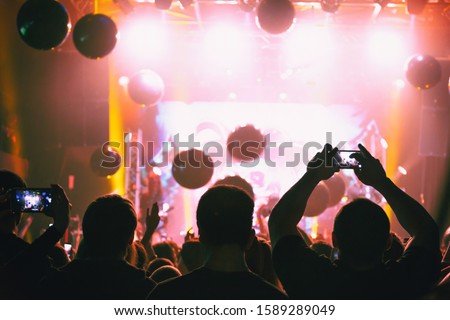 Viewers shoot video on a smartphone at a concert.