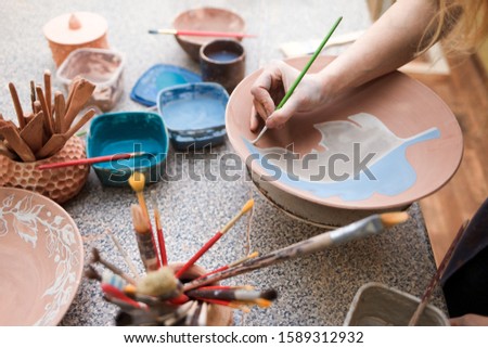 Potter woman paints a ceramic plate. Girl draws with a brush on earthenware. Process of creating clay products
