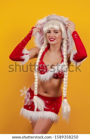 Beautiful emotional young girl dressed as Santa Claus and with long braids hairstyle posing on a yellow background