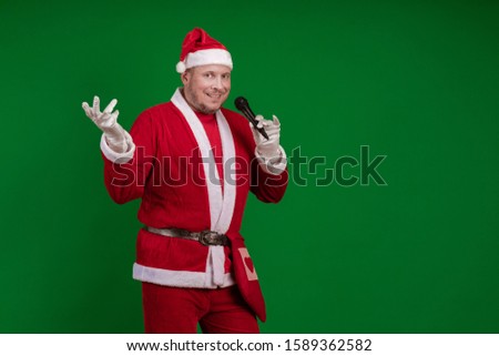 Emotional Santa Claus holds a microphone in his hands, sings and poses on a green background