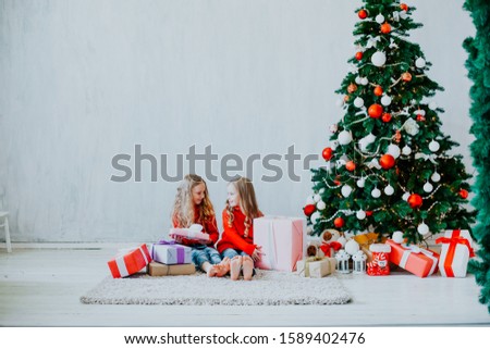 two little girls opens Christmas gifts at the Christmas tree new year holiday house