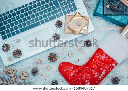 Flat lay or top view of laptop keyboard, gifts and red Santa Claus sock on fake snow. Online shopping for christmas holiday concepts.