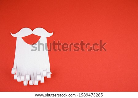 White paper beard on a red background. The concept of Christmas and New Year holidays.