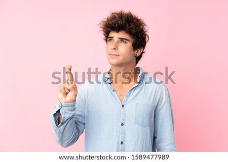 Young caucasian man with jean shirt over isolated pink background with fingers crossing and wishing the best