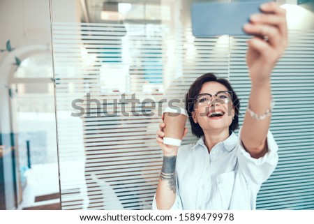 Waist up of smiling lady using smartphone in office stock photo