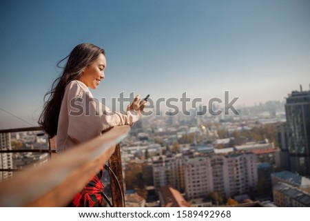 Waist up of happy attractive girl using smartphone while staying on roof stock photo