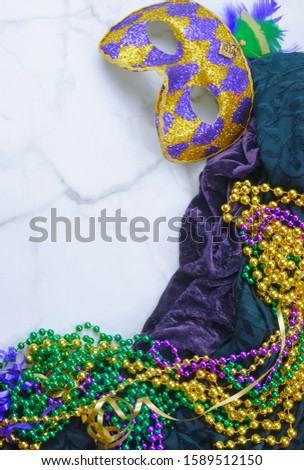 Mardis Gras border on marble background includes harlequin mask with green, gold and purple beads and matching fabrics. Copy space