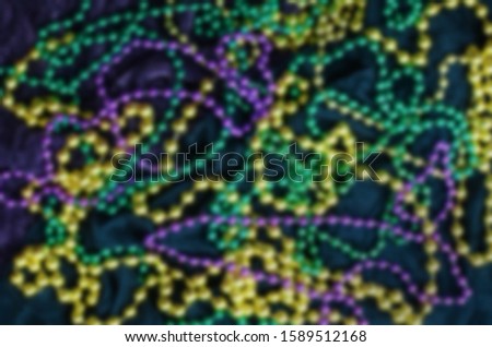 Mardi Gras background blur image of green, gold and purple beads on green and purple fabric.