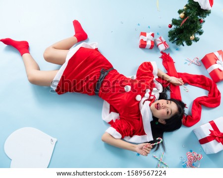 Asian teenager girl wearing Santa Claus costume lying on floor with Christmas tree and gift boxes.