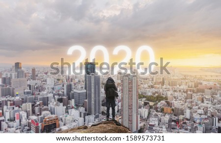 New year and New day concept. a man standing on peak looking city sunrise with 2020 in the city