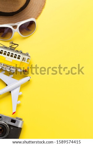 Travel concept with camera, sun hat, sunglasses, tram and airplane toy over yellow sunny backdrop. Top view flat lay with copy space