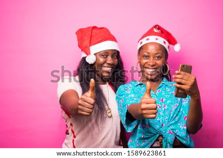 young black African women wearing Xmas hat standing on a pink background excited doing  thumps up sign 