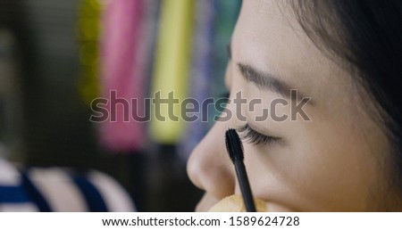 close up portrait of beautiful female model face. Makeup artist hands applies mascara to eyelashes of asian girl on backstage. make up master painting in process on blurred view of dressing room.