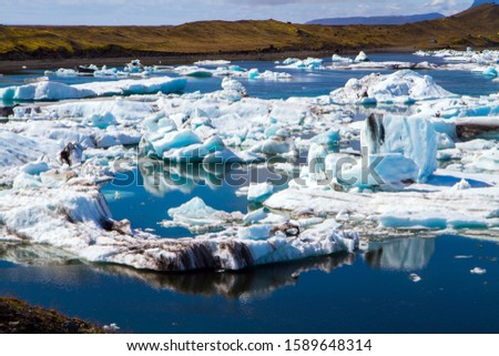 Cold day in July. Iceland. The lagoon Jokulsaurloun. The ice is covered in volcanic ash. White and blue icebergs and ice floes reflected in the water. The concept of northern and photo tourism
