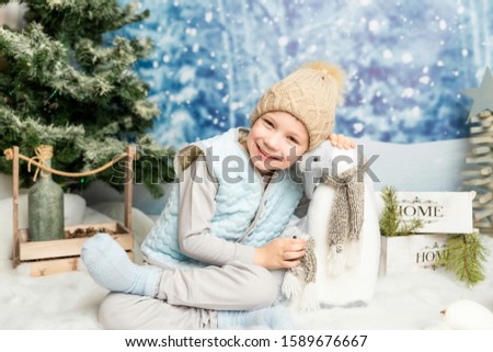 Little boy sitting with soft toy penguin on winter decorated background