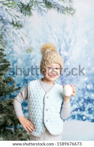 smiling little boy in winter clothes playing with a snowball in his hand