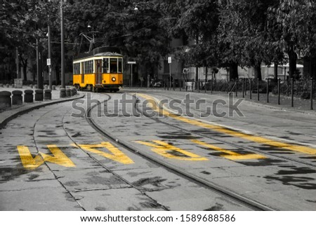 A picture of the typical yellow tram in Milan, Italy, passing throught the city center. The tram is isolated in the black and white background. 
