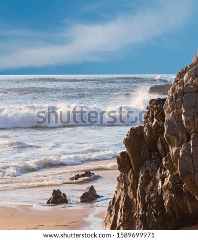 fragment of a sandy beach with a moving sea wave and a picturesque rock in the foreground near the Portuguese city of Sintra