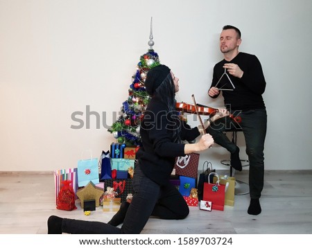 young woman and attractive man playing musical instruments near christmas tree