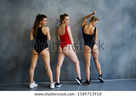 Back view of professional female gymnasts with ponytail and wearing sportswear posing for photograph next to studio wall within photoshoot 