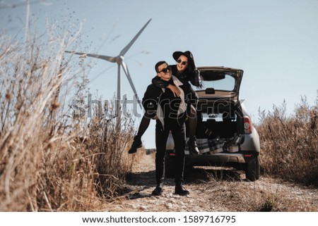 Happy Traveling Couple Enjoying a Car Trip on the Field Road with Electric Wind Turbine Power Generator on the Background