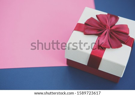 White Christmas present box with red ribbon on pink & blue paper backgrounds.Decorative New Year gift box in close up
