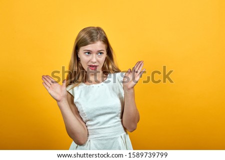 Charming shocked blonde young woman spreads hands, looking confused over isolated orange background wearing white shirt. Lifestyle concept