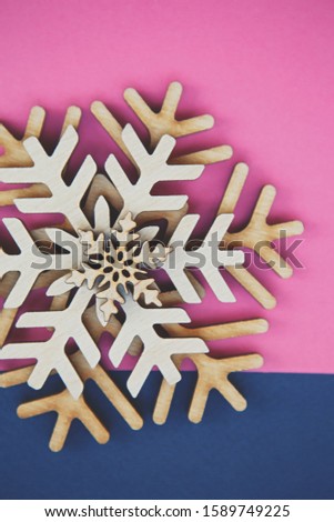 Flat lay vertical background with Christmas toys.Wooden rustic snowflakes on pink and blue paper backgrounds shot directly from above.Beautiful hand made crafts for winter holidays