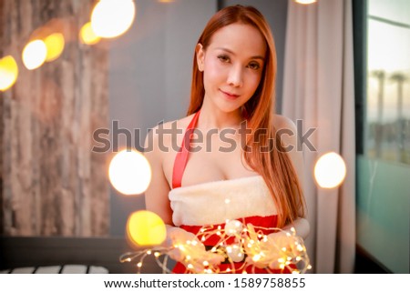 Merry Christmas and Happy New Year! Young woman in wear dress Santa Claus and with decorative lights lie in her bed.