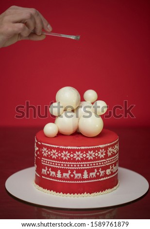 Christmas cake decorated with sweet figures of Christmas tree and deer. Red-white cake with different white balls. 