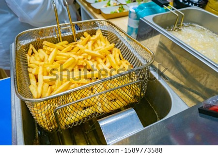 French fries. Work with a deep fryer. Hot oil. Oil drains from potatoes. Cooking french fries. Work in a restaurant. Fast food restaurant. Concept - harmful food. Snack. Cafe. Crispy potato Royalty-Free Stock Photo #1589773588